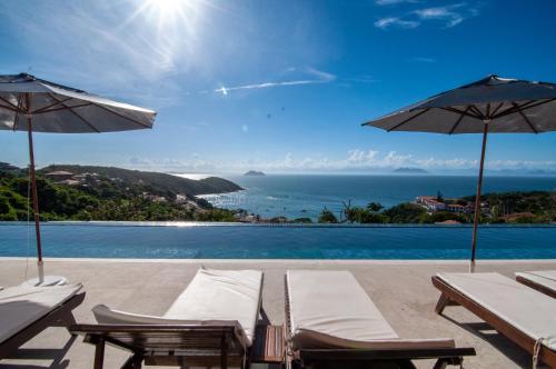a pool with chairs and umbrellas and the ocean at Buzios Mar Hotel in Búzios