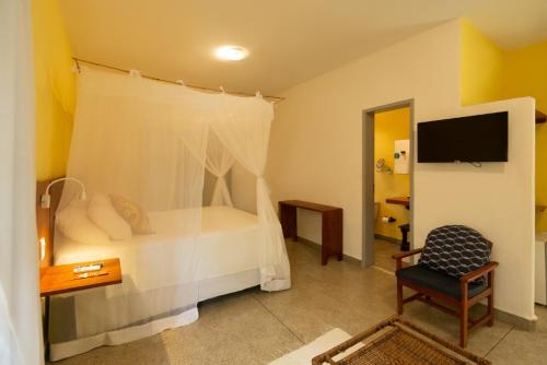 a bedroom with a bed and a chair and a television at Travel Inn Trancoso Suítes in Trancoso