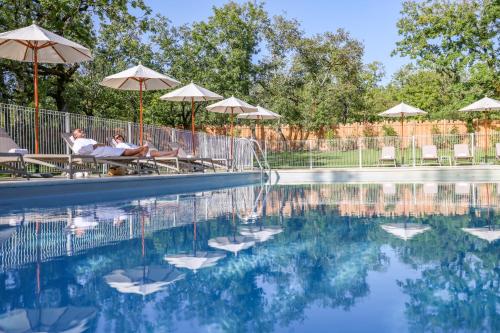 two people sitting under umbrellas near a swimming pool at Le Bois d'Imbert in Rocamadour