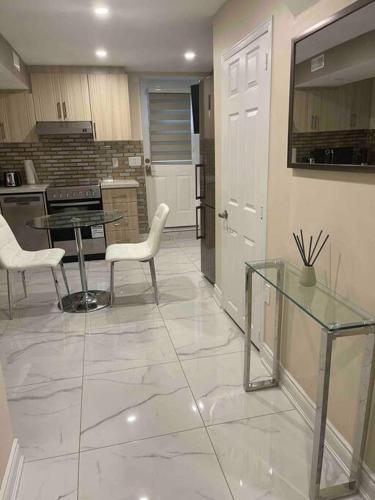 uma cozinha com uma mesa de vidro e cadeiras brancas em Adorable1-Bedroom Basement apartment, free parking em Brampton