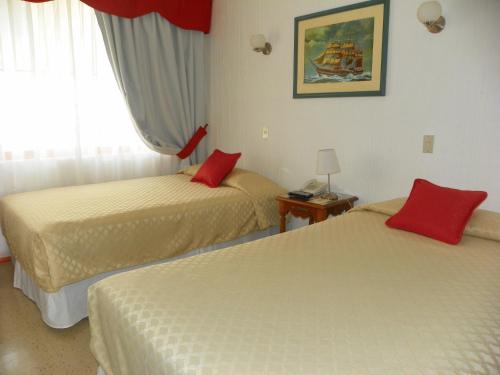 two beds in a hotel room with red pillows at Hotel Savona in Arica