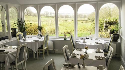 um restaurante com mesas e cadeiras brancas e janelas em The Old Rectory em Coniston