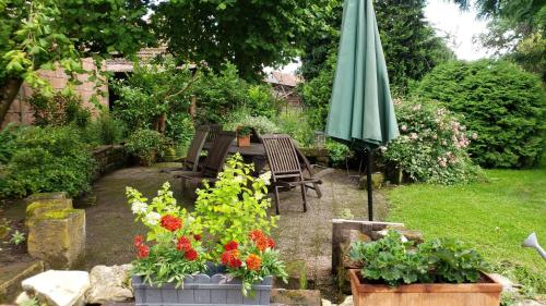 a garden with a table and an umbrella and flowers at GITE AU PETIT RUISSEAU-Etage et combles-maison alsacienne 4 personnes 4 nuitées minimum in Langensoultzbach