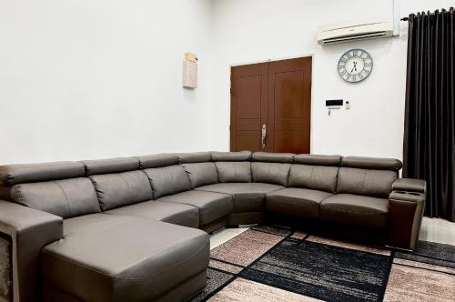 a brown leather couch in a room with a clock on the wall at Bandar Melaka Family Bungalow Private Pool BBQ WiFi Netflix in Melaka