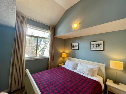 a bedroom with a bed with a checkered blanket and a window at Mountain Chalet at Mystic Springs, 2BR, 2BA, Heated Pool, Hot Tub! in Canmore