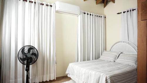 a bedroom with a bed with white curtains and a fan at Villa Rosalía Jarabacoa con Piscina Climatizada in Jarabacoa