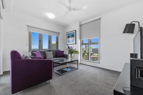 a living room with a purple couch and windows at H on Mitchell Apartment Hotel in Darwin