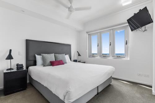a white bedroom with a large bed and a window at H on Mitchell Apartment Hotel in Darwin
