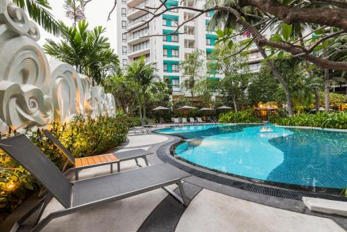 a large swimming pool with benches and trees and buildings at Chatrium Sathon Bangkok in Bangkok