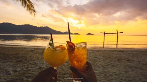 a person holding two drinks in front of the beach at Peninsula Beach Resort in Ko Chang