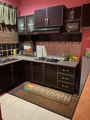 a kitchen with black cabinets and a kitchen rug at Idaman Sinar Homestay in Nibung Tebal