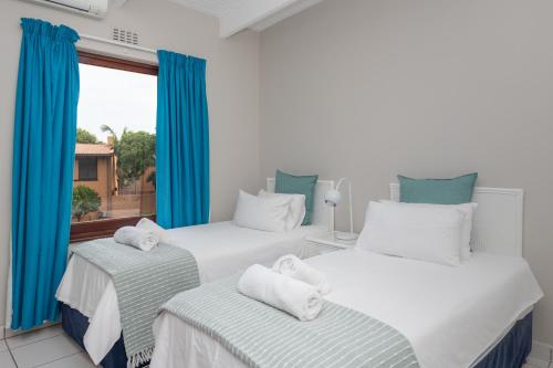 two beds in a room with blue curtains and a window at San Lameer Villa 2823 - 3 Bedroom Classic - 6 pax - San Lameer Rental Agency in Southbroom