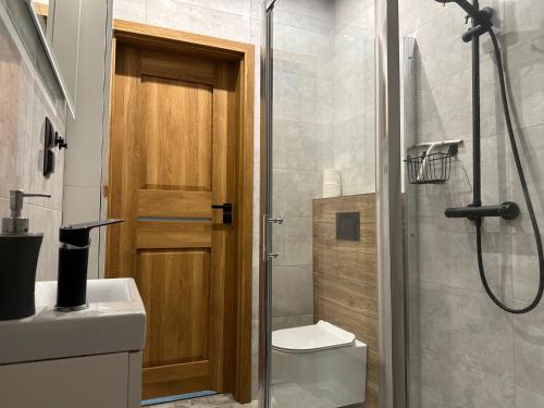 ein Badezimmer mit einer Dusche, einem WC und einer Holztür in der Unterkunft Apartament nad Jeziorem in Skorochow