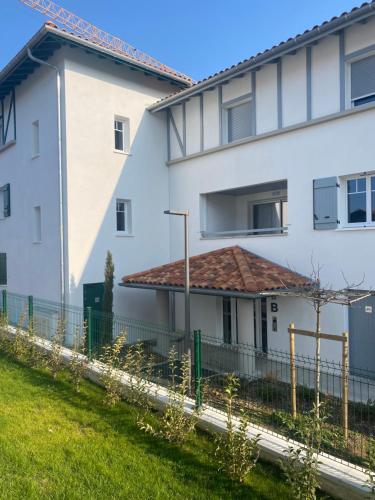 a white building with a fence in front of it at CHAMBRE D'HÔTE COSY Hiriburu in Saint-Pierre-dʼIrube
