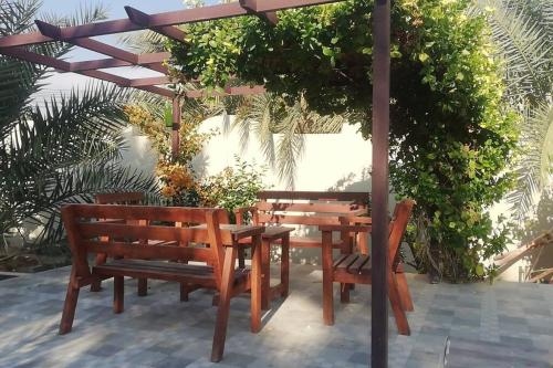 una mesa de madera y bancos bajo una pérgola en استراحة شرفة الواحةOasis Terrace Inn and Lounge, en Bahlāʼ