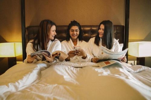 three women sitting on a bed reading a newspaper at Grand Mercure Bangalore - An Accor Brand in Bengaluru