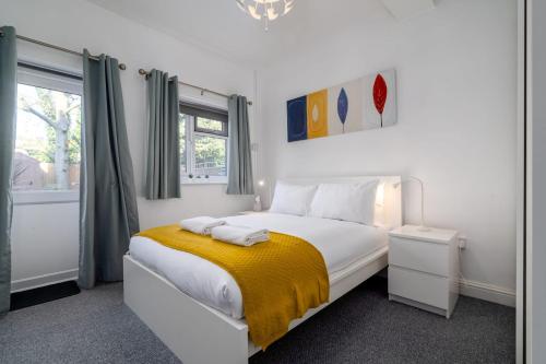 a white bedroom with a bed with a yellow blanket at GuestReady - Superb modern with garden in Kilburn in London