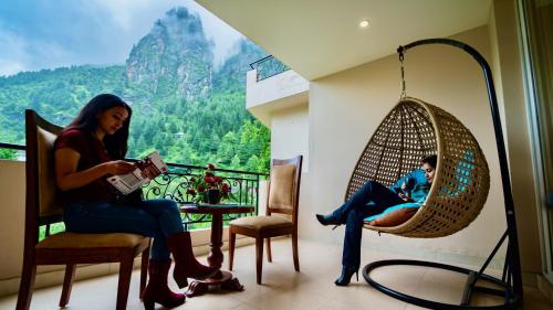Dos mujeres sentadas en un balcón leyendo un libro en The Allure Grand Resort - A Riverside Resort and Spa, en Manali