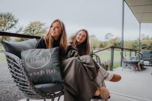 dos chicas sentadas en una silla de mimbre en un porche en Comeragh Pods en Kilmacthomas