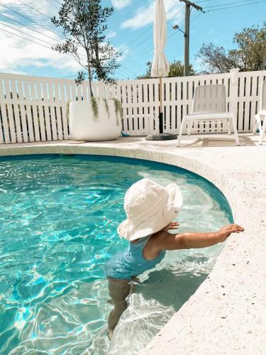 a child wearing a hat standing in a swimming pool at The Villa's Mooloolaba in Mooloolaba