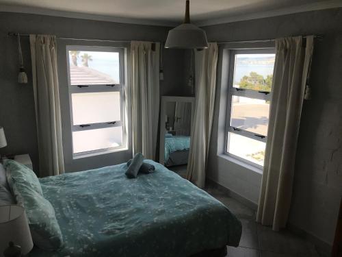 a bedroom with two large windows and a bed at The Whale Tale Villa in St Helena Bay
