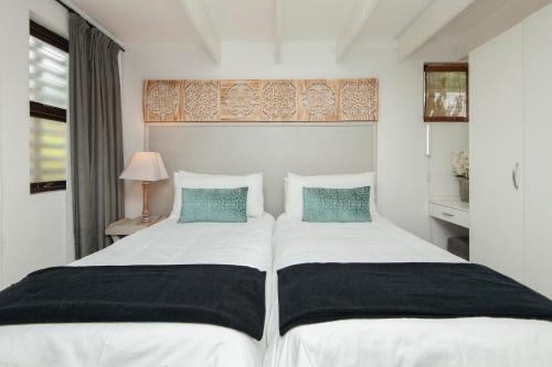 a bedroom with two beds with white sheets and blue pillows at Windsong Cottage in Hermanus