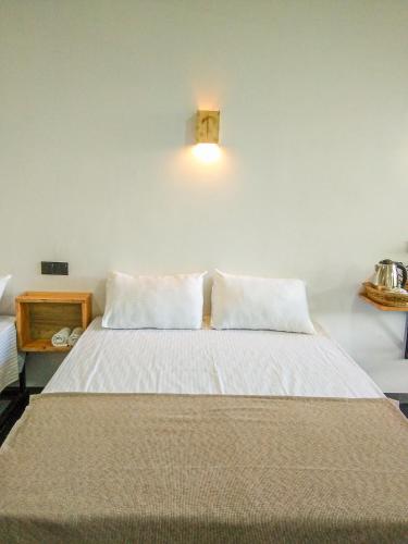 a bed with white sheets and a light on the wall at Crystal Resort in Badulla