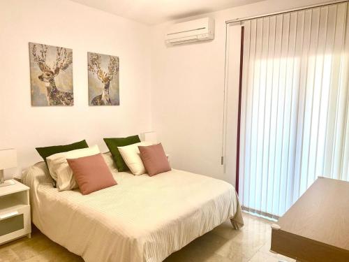 a white bedroom with a bed with pink and green pillows at PalmMar Balandros Deluxe By Deihu Experiences in Palm-mar