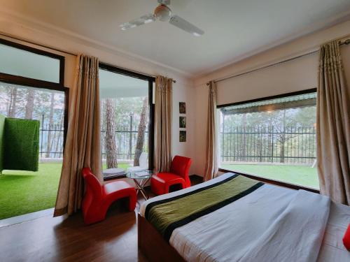 a bedroom with a bed and two red chairs and large windows at Hotel Bliss in Kasauli