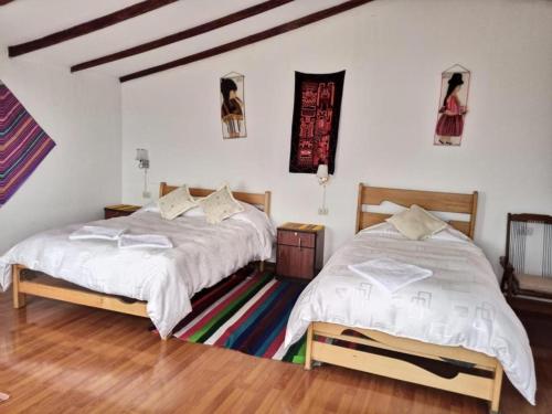 Habitación con 2 camas, paredes blancas y suelo de madera. en Hostal Inca Uma, en Comunidad Yumani