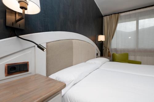 a bedroom with a white bed with a lamp and a chair at Hotel de Montaña El Mirador in Broto