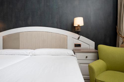 a bedroom with a white bed and a green chair at Hotel de Montaña El Mirador in Broto