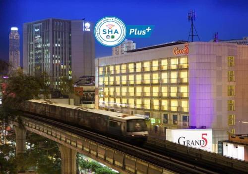 a train on a track in a city with a building at Grand 5 Hotel & Plaza Sukhumvit Bangkok in Bangkok