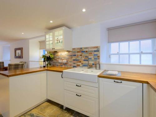 eine Küche mit weißen Schränken, einem Waschbecken und einem Fenster in der Unterkunft Curlew in North Berwick
