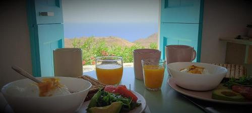 stolik z miskami z jedzeniem i dwie szklanki soku pomarańczowego w obiekcie WabiSabi Serifos Chora w/ Spectacular Sea Views w mieście Serifos Chora