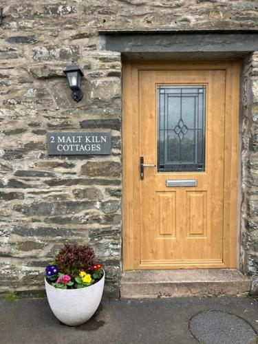 uma porta de madeira e um vaso de flores em frente a um edifício em 2 Malt Kiln Cottages em Grizebeck