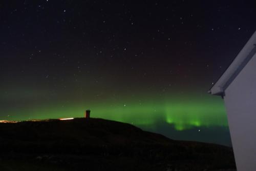 an aurora in the sky with a lighthouse on a hill at Malin Head SolasTobann ArtHouse Room 1 En-suite in Malin Head