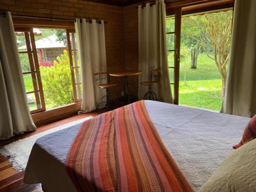 a bedroom with a bed and a large window at Pousada Bosque do Visconde in Visconde De Maua