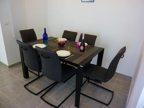 a dining room table with black chairs and a black table with plates and bottles at Appartement chaleureux à Penta-di-Casinca 60 m² avec piscine privée in Penta-di-Casinca