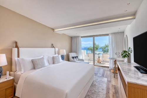 a white bedroom with a large bed and a television at Domes Miramare, a Luxury Collection Resort, Corfu - Adults Only in Moraitika