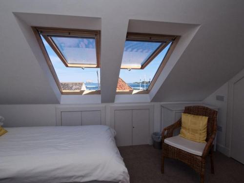 a bedroom with three windows and a bed and a chair at Quayside Cottage in North Berwick