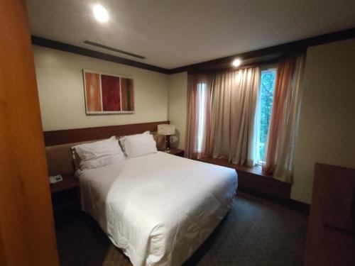 Habitación de hotel con cama blanca y ventana en Privilege Apart hotel Mountain Village, en Canela