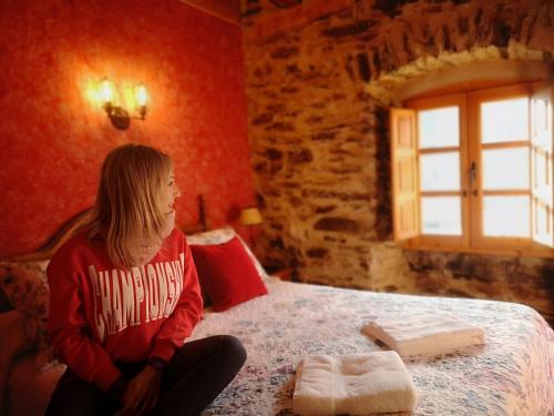 a woman sitting on a bed in a room at Hotel Rural LA CÁRCEL in Murias de Paredes