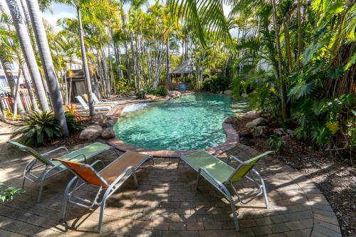 a swimming pool with chairs and palm trees at The Beach Motel Hervey Bay in Hervey Bay