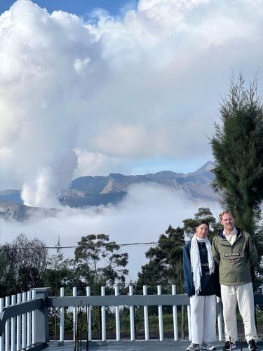 two people standing next to a white fence with a view of a lake at Cahyo Homestay Bromo in Bromo