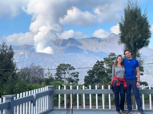 a man and a woman standing next to a fence with a eruption at Cahyo Homestay Bromo in Bromo