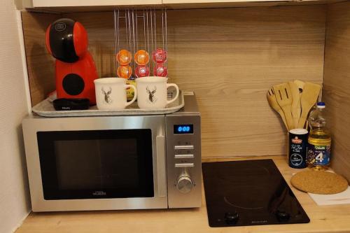 un four micro-ondes assis sur un comptoir avec des tasses et des ustensiles dans l'établissement Sur les toits, studio centre-ville, WIFI Netflix, à Montbéliard