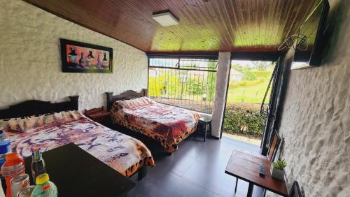 a bedroom with two beds and a table and a window at Hospedaje campestre los pinos in Guatavita