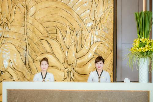 two women standing behind a counter in front of a wooden wall at Muong Thanh Grand Bac Giang Hotel in Bắc Giang