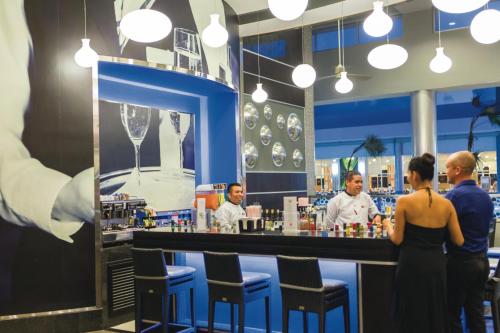 a group of people standing at a bar in a restaurant at Riu Playacar - All Inclusive in Playa del Carmen